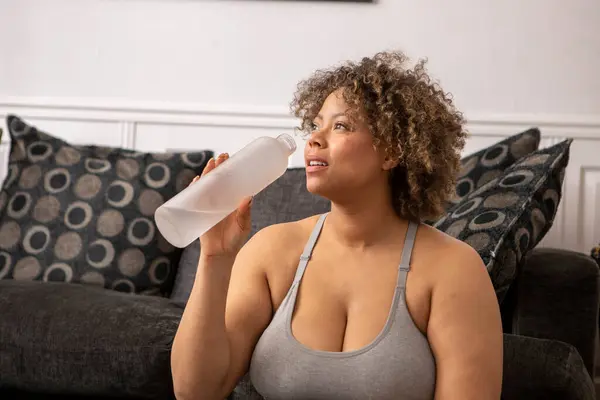 Woman with water bottle after workout in living room