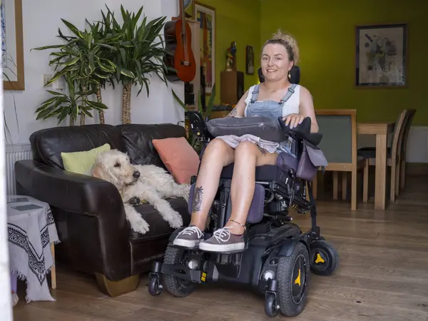 Elektrikli sandalyedeki kadın ve köpek oturma odasında.