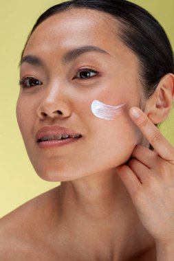 Studio shot of woman applying face cream on cheek