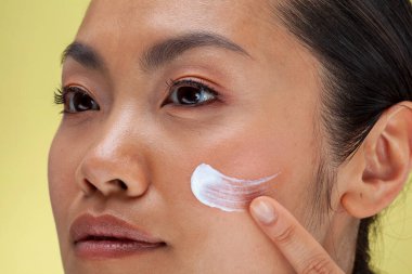 Close-up of woman applying face cream on cheek