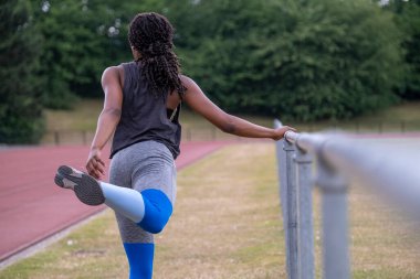 Koşu pistinde bacağını esneten atletik bir kadın.