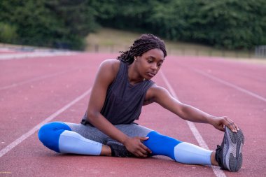Atletik kadın koşu pistinde bacak esnetiyor