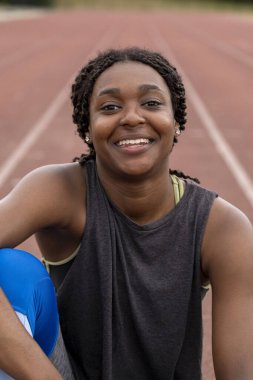 Koşu pistinde oturan gülümseyen atletik kadın portresi