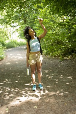 Genç bir kadın ormanda yürüyor, ağaçlara bakıyor.