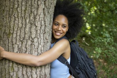 Genç bir kadın ormanda yürüyüş yapıyor, ağaca sarılıyor.