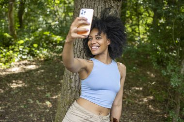 Ormanda selfie çekmek için akıllı telefon kullanan genç bir kadın.