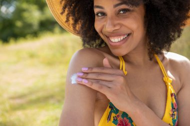 Güneş kremi sürerken yaz şapkası takan genç bir kadının portresi.