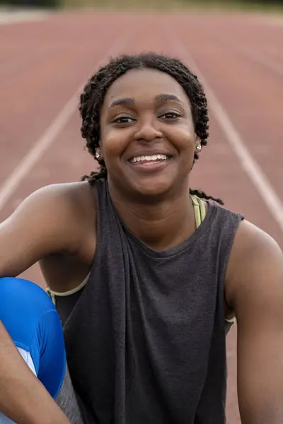 Koşu pistinde oturan gülümseyen atletik kadın portresi