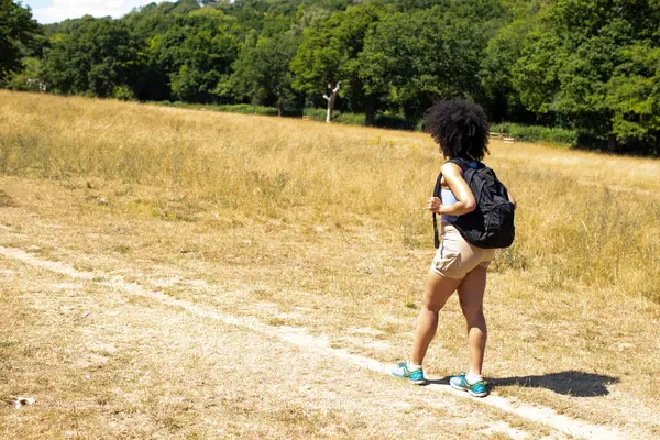 Sırt çantalı genç bir kadın kırsalda yürüyüş yapıyor.