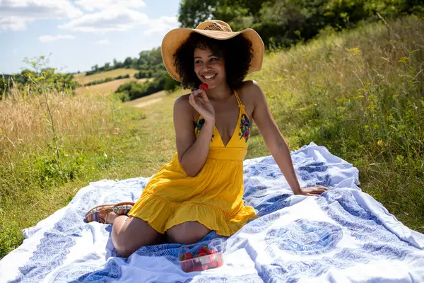 Genç kadın çayırda battaniyede oturuyor.