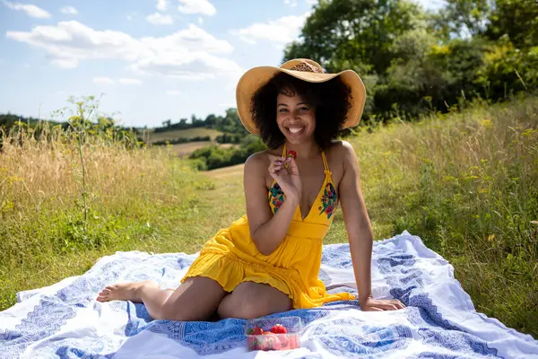 Genç kadın çayırda battaniyede oturuyor.