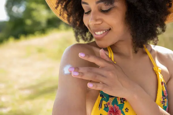 Güneş kremi sürerken yaz şapkası takan genç bir kadın.