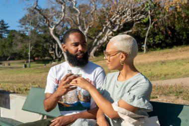 Çift bankta oturuyor ve su içiyor.