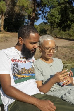 Çift bankta oturuyor ve akıllı telefon kullanıyor.