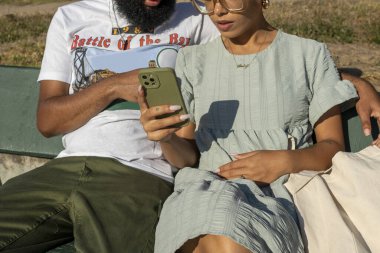 Çift bankta oturuyor ve akıllı telefon kullanıyor.