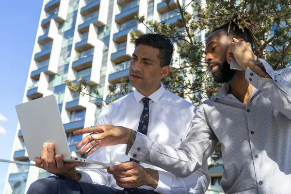 İki iş adamı iş bölgesinde dizüstü bilgisayar kullanıyor ve telefonla konuşuyor.