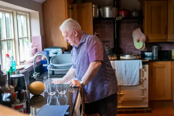 Yaşlı adam evde bulaşık yıkıyor.