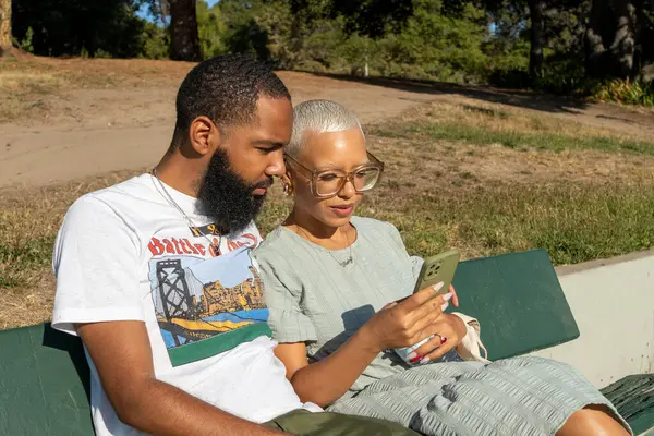 Çift bankta oturuyor ve akıllı telefon kullanıyor.