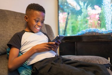 Akıllı telefonlu çocuk kanepede oturuyor.