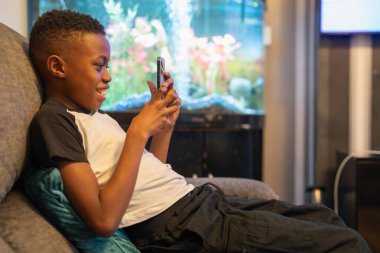 Akıllı telefonlu çocuk kanepede oturuyor.