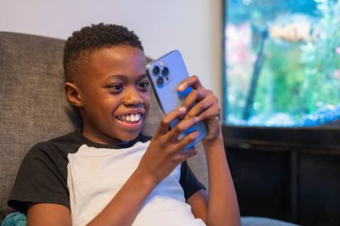 Akıllı telefonlu çocuk kanepede oturuyor.