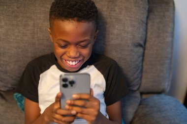 Akıllı telefonlu çocuk kanepede oturuyor.