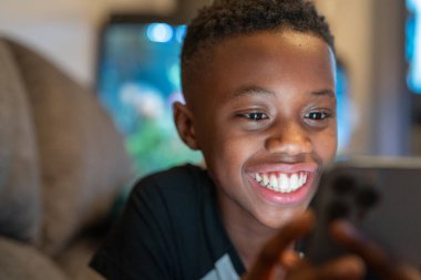 Akıllı telefonlu çocuk kanepede oturuyor.