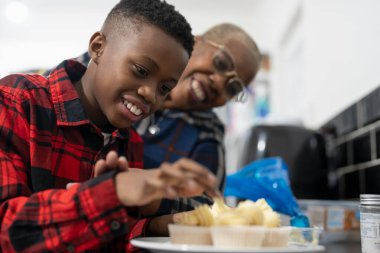 Grandson and grandmother preparing cupcakes in kitchen 