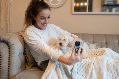 Woman with dog on sofa, using smartphone