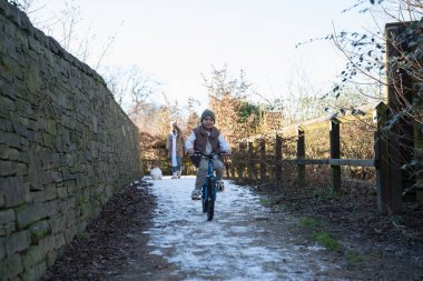 Boy (6-7) riding bike down snowy path
