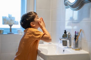 Boy (6-7) washing face in bathroom