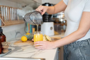 Woman in kitchen, pouring freshly made smoothie, midsection