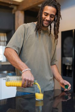 Man with dreads pouring orange juice into glass in kitchen
