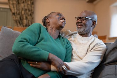 Gülümseyen yaşlı çift kanepede sarılıyor.