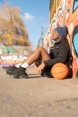 Duvarda duvar yazısıyla kaplı futbol topuyla oturan adam.