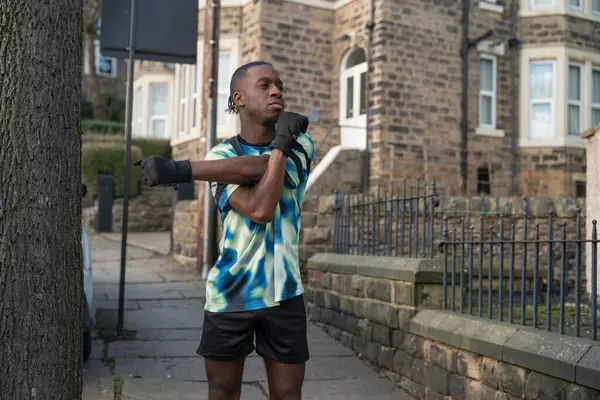 Erkek sporcu kaldırımda kol esnetiyor.