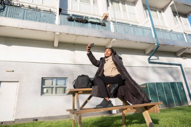 Piknik masasında oturup selfie çeken gülümseyen kadın portresi.