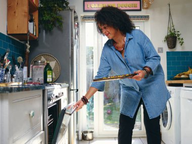 Kadın fırına yemek koyuyor.