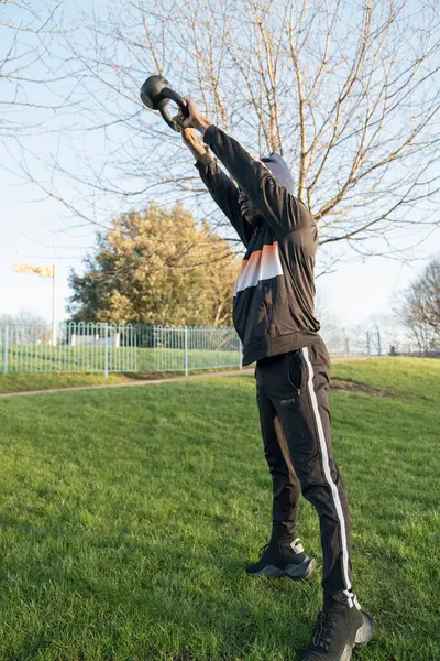 Atletik adam parkta kettlebell salıncak egzersizi yapıyor.