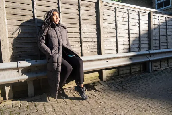 Uzun paltolu bir kadının portresi çitin parmaklıklarında oturuyor.