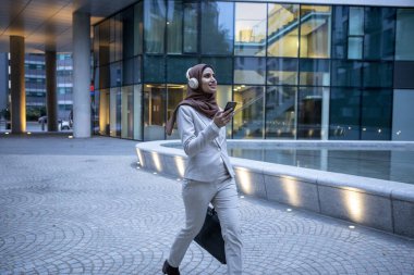 İngiltere, Londra, tesettürlü iş kadını ve şehirde yürüyen kulaklıklar