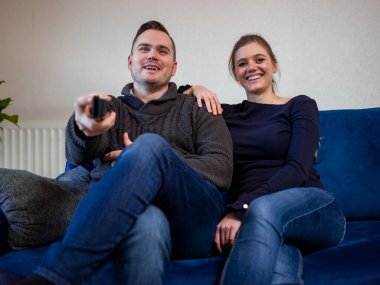 Kanepede televizyon izleyen gülümseyen çift.