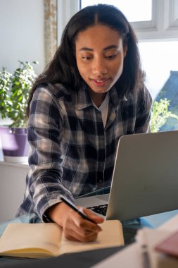 Evde dizüstü bilgisayar kullanan genç bir kadın.