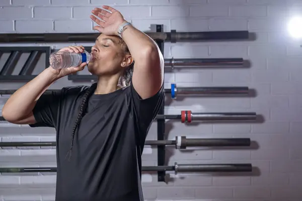 Spor salonunda biberondan su içen yorgun bir kadın.