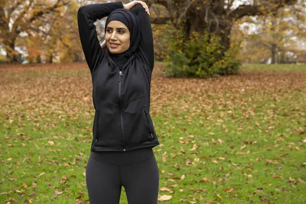 Siyah spor elbiseli ve tesettürlü kadın parkta geriniyor.