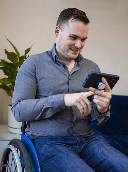Tekerlekli sandalyedeki gülümseyen adam evde akıllı telefondan video görüşmesi yapıyor.