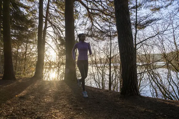 Genç bir kadın ormanda koşuyor.