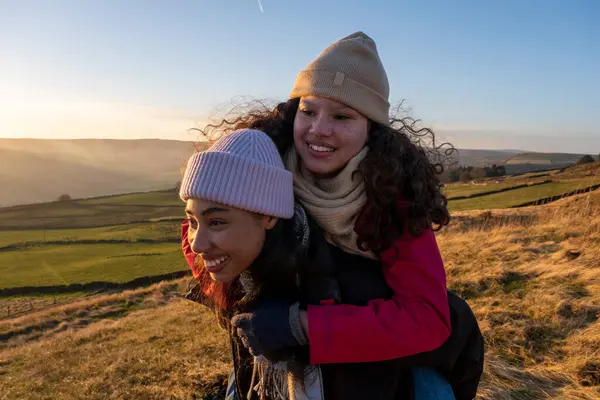 Genç bir kadın kırsal alanda arkadaşını sırtında taşıyor.