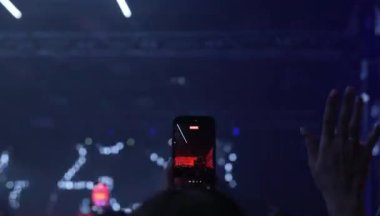 Fan cep telefonuyla müzik konseri performansı çekiyor. Mavi neon ışıklar. 8K görüntü. Taraftarlar DJ konserini canlı çekiyor.