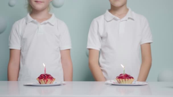 男孩和女孩的生日 他们带着纸杯蛋糕和蜡烛 吹着蜡烛 彼此深情地看着对方 穿着一件白色的T恤 — 图库视频影像